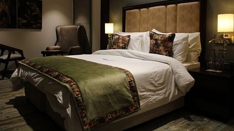 Side view of the bedroom with multiple pillows arranged on the bed and a huge chair next to it at BluSalzz Residence, Amritsar